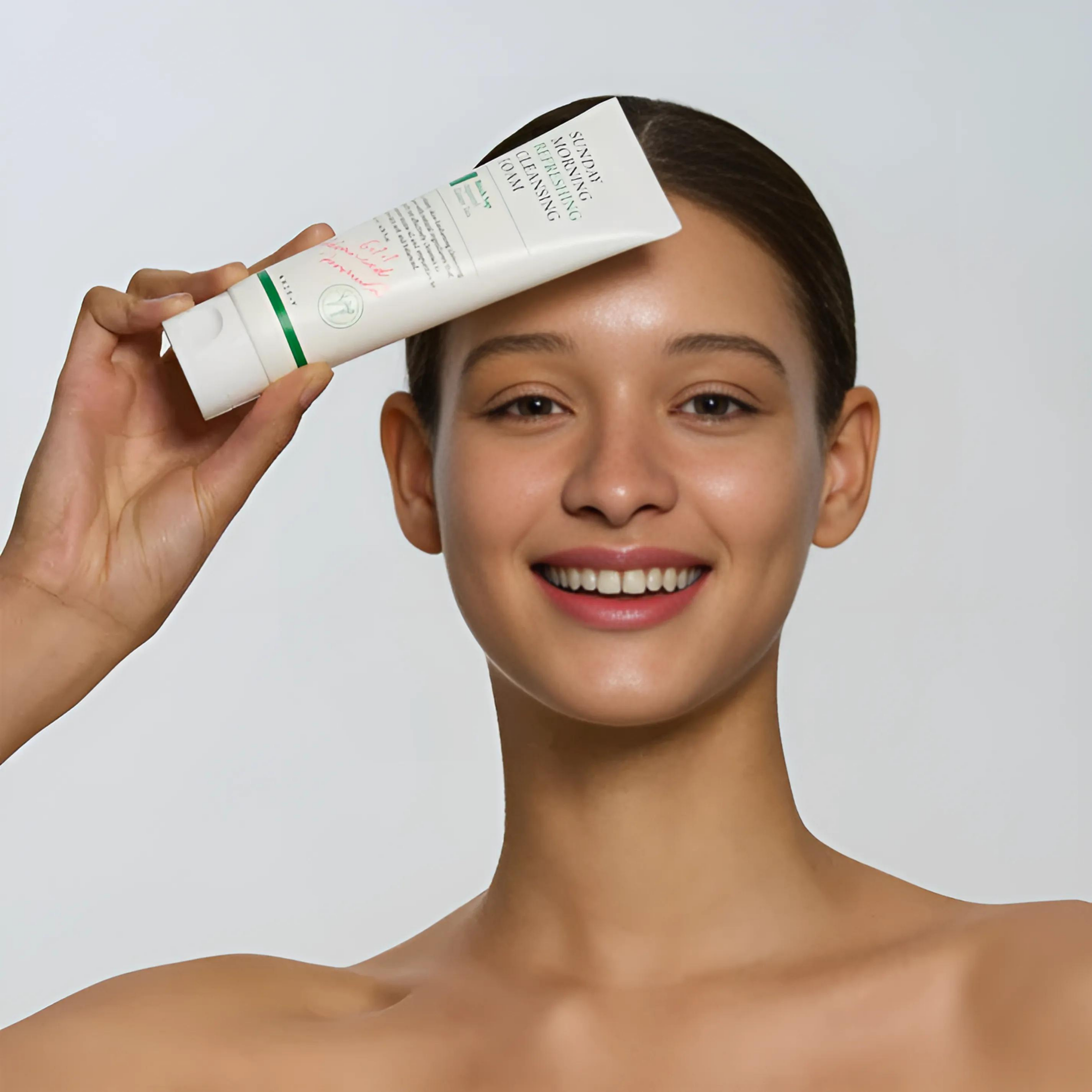 Woman holding a skincare product above her face against a plain background