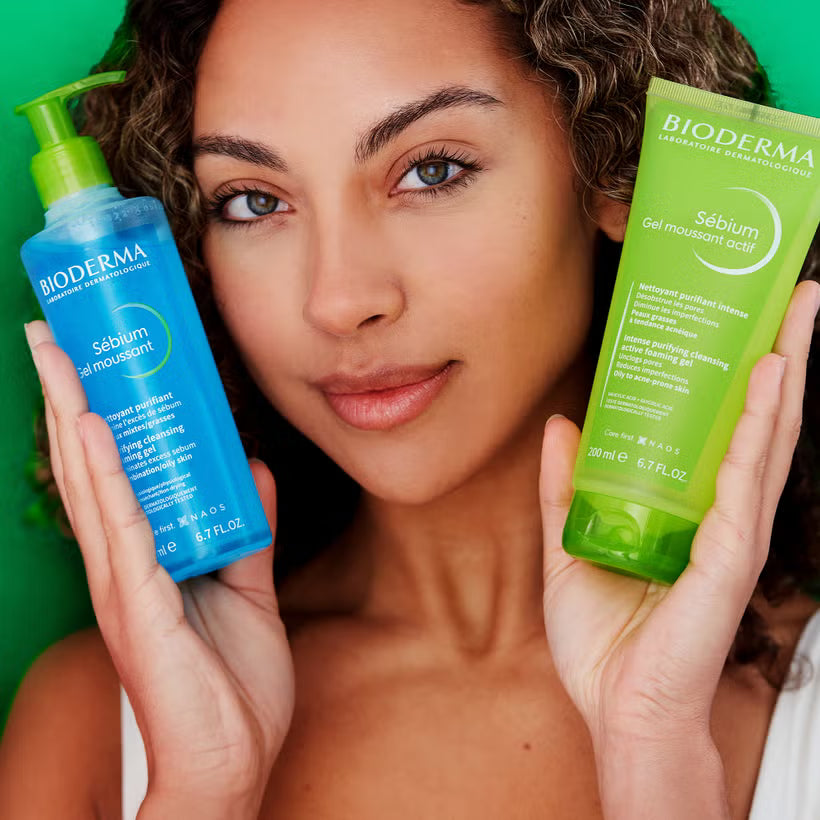 Woman holding Bioderma skincare products against a green background